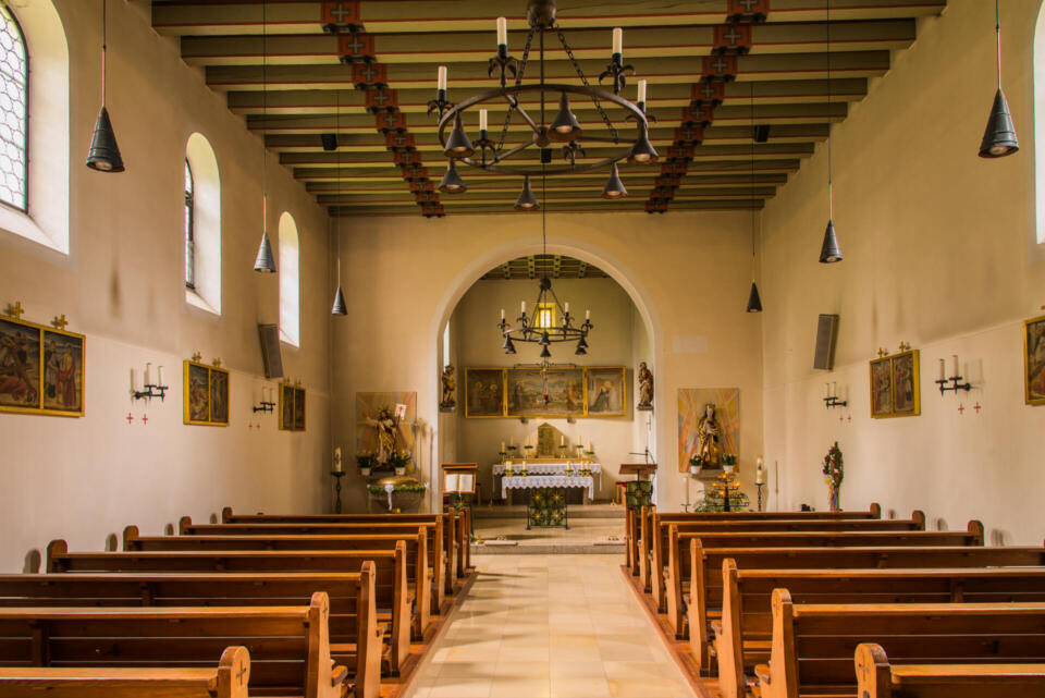 Innenansicht des Kirchenraums heute, mit Sitzbänken und Blick zum Altar.